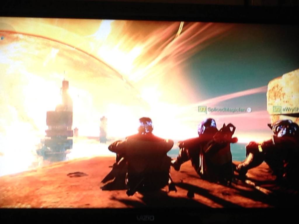 A photo of a TV screen showing 3 guardians sitting on the balcony of the Lighthouse on Mercury, admiring the sun.